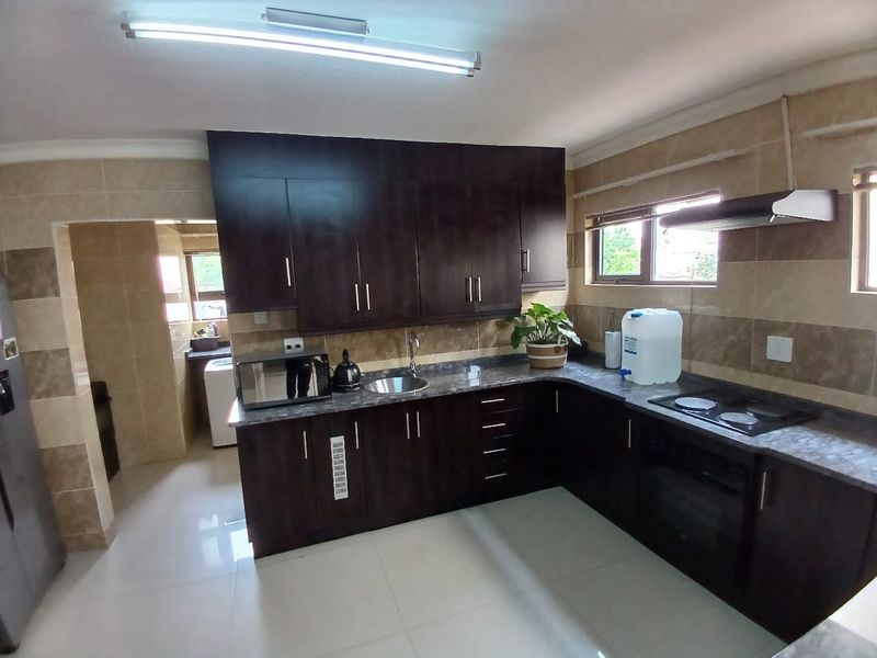 A functional kitchen featuring dark wood cabinetry, granite countertops, built-in oven, electric hob, and tiled splashbacks, with an adjacent scullery area.