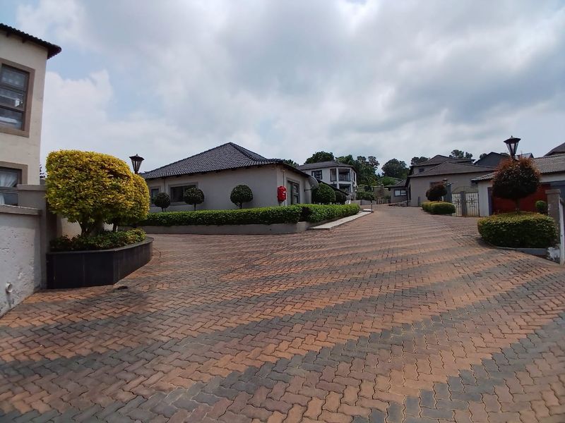 A view of the paved driveway and exterior facade of the townhouse complex, featuring well-maintained landscaping and paved access paths.