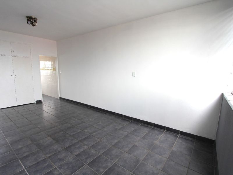 An empty living area featuring dark tiled flooring, built-in storage cupboards, and venetian blinds, offering a clean and neutral space ready for customization.
