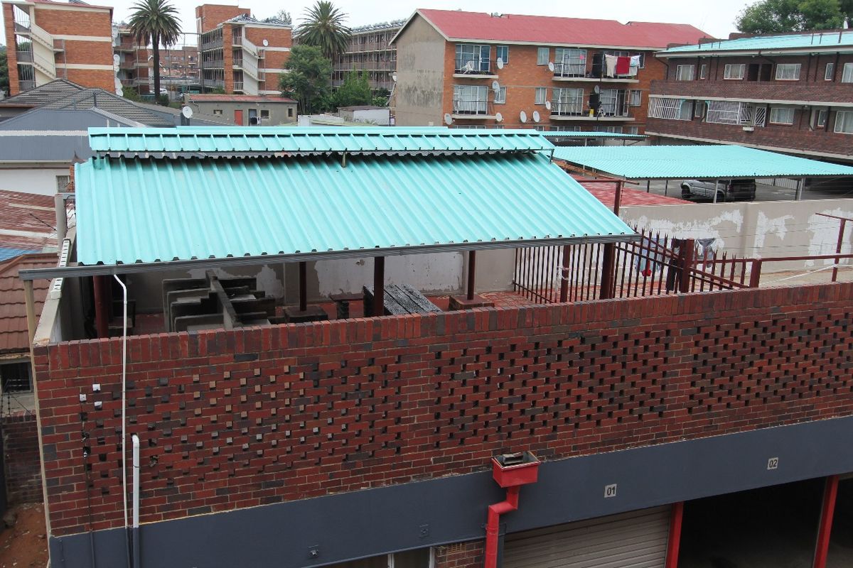 An elevated view of a rear courtyard area featuring a covered patio with a corrugated metal roof and brick boundary walling.