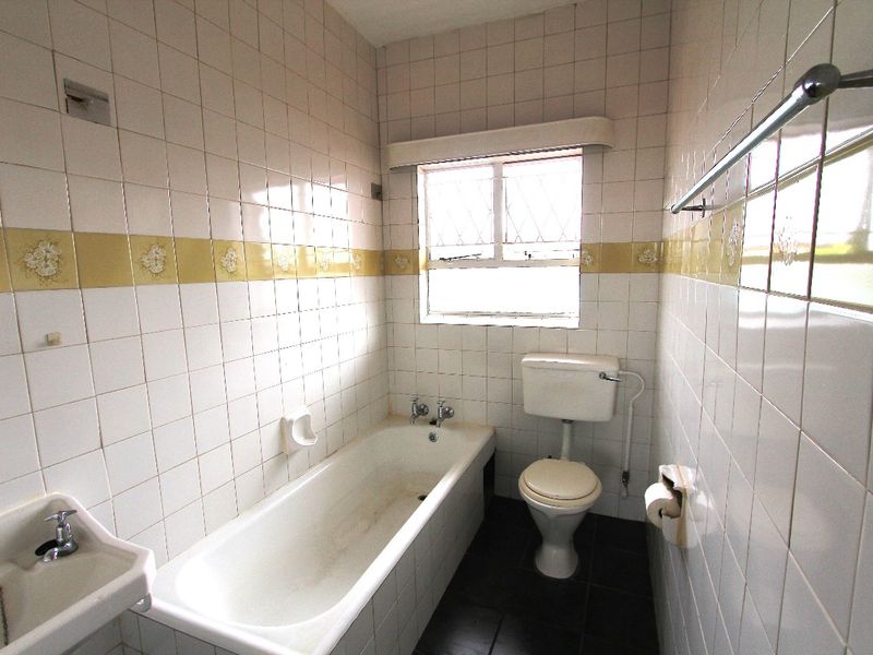 A dated bathroom featuring a standard bathtub, toilet, and wall-mounted basin with original tiled finishes throughout.