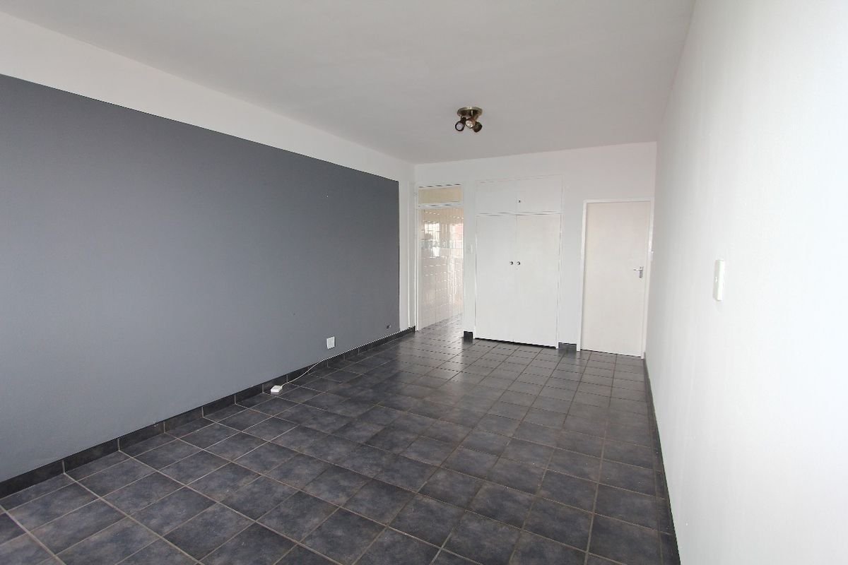 An empty bedroom featuring dark tiled flooring, a grey accent wall, and built-in storage cupboards.