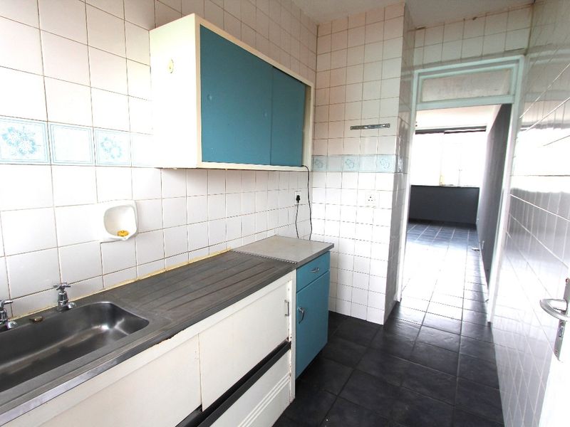 A compact, dated kitchen featuring tiled walls, built-in cabinetry, and a stainless steel sink, offering potential for a modern renovation.