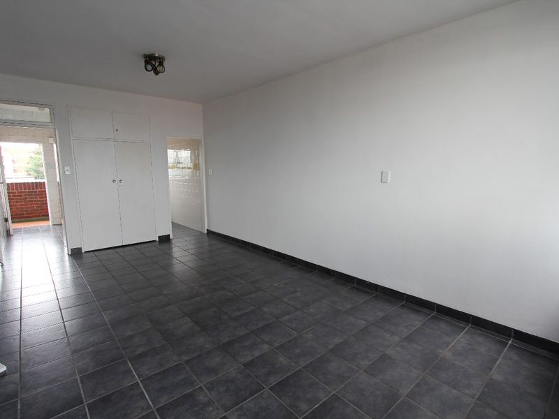 An empty living room featuring dark tiled flooring, built-in storage cupboards, and access to an adjoining balcony area.