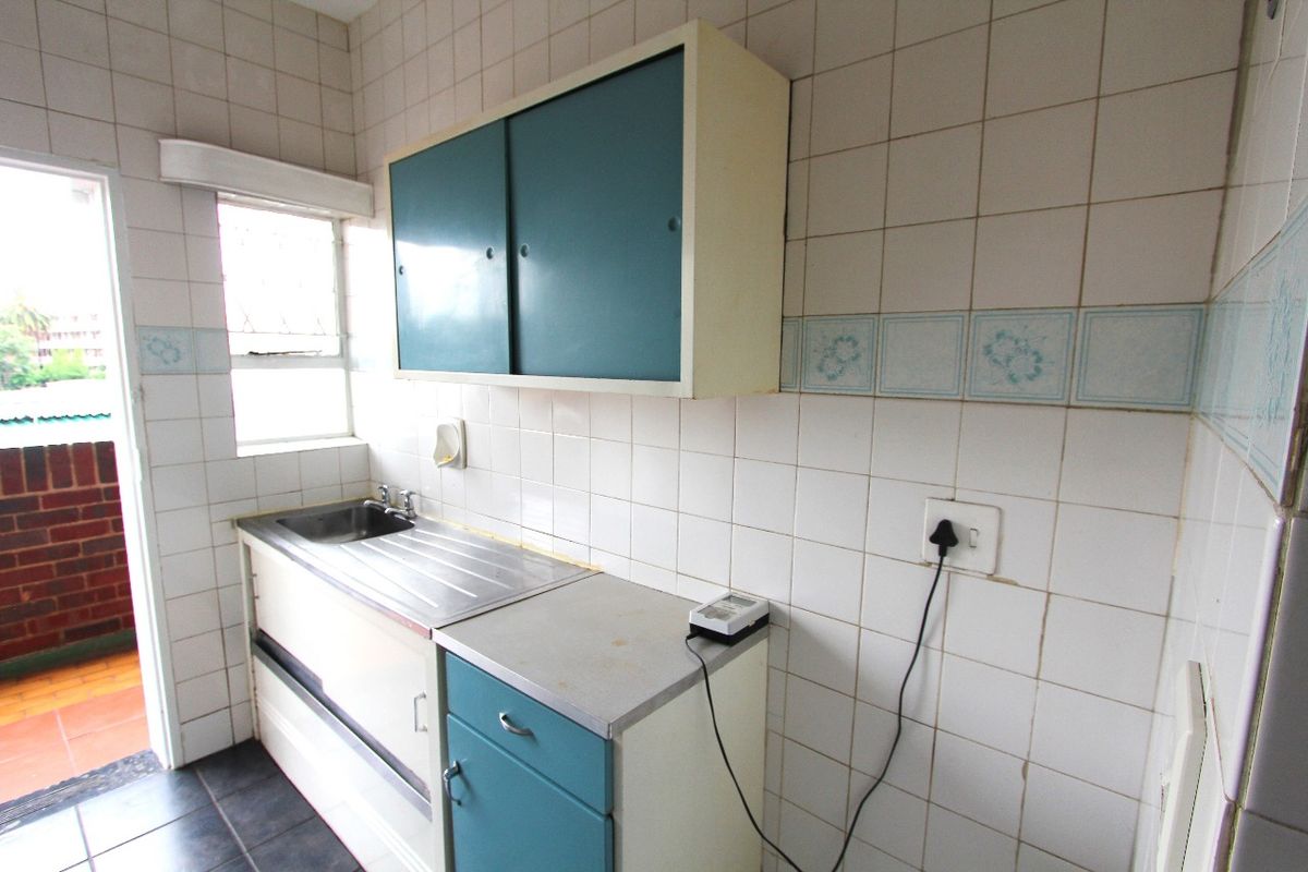 A compact, dated kitchen area featuring original cabinetry, a stainless steel sink, and tiled wall finishes, offering potential for a modern renovation.