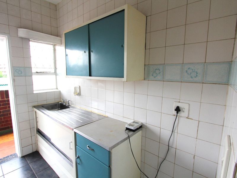 A compact, dated kitchen area featuring original cabinetry, a stainless steel sink, and tiled wall finishes, offering potential for a modern renovation.