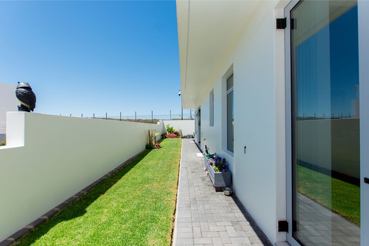 A well-maintained rear exterior area featuring a paved walkway, a neat lawn, and a secure boundary wall with access via a sliding glass door.
