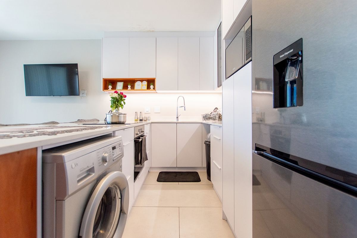 Modern kitchen featuring sleek white cabinetry, stone countertops, integrated appliances, and under-cabinet lighting, creating a clean and functional culinary space.