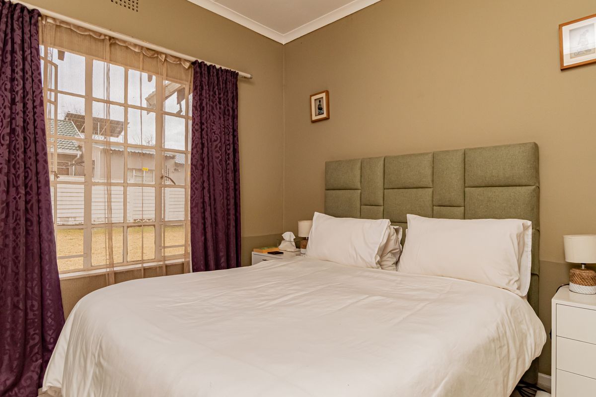 A comfortable bedroom featuring a grid-pattern window and neutral wall tones, providing a functional and well-lit sleeping space.