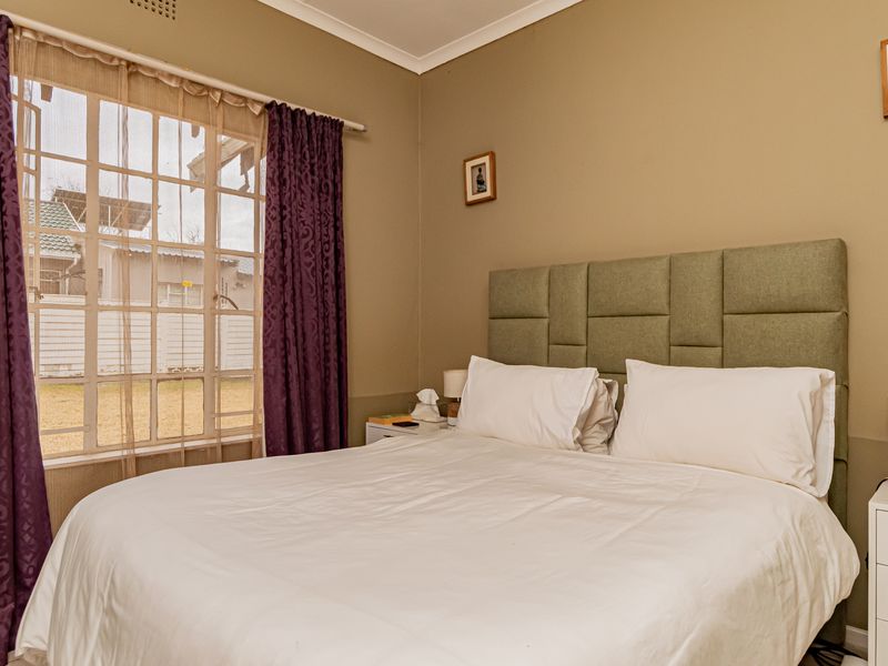 A comfortable bedroom featuring a grid-pattern window and neutral wall tones, providing a functional and well-lit sleeping space.