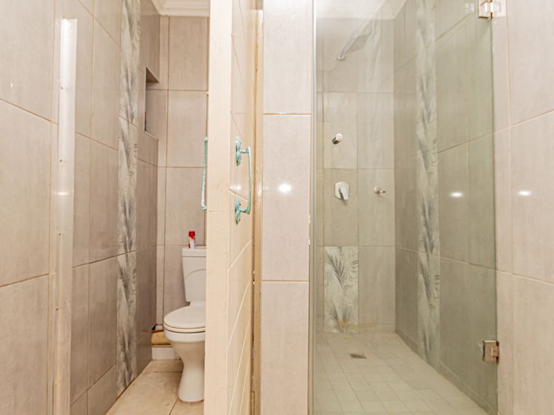 A functional bathroom featuring a glass-enclosed shower and a separate toilet area with neutral ceramic wall tiling.