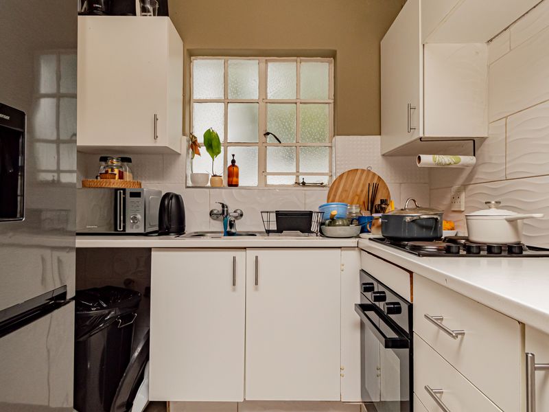 Compact kitchen featuring white cabinetry, laminate countertops, a built-in oven with gas hob, and a tiled backsplash with a window for natural light.