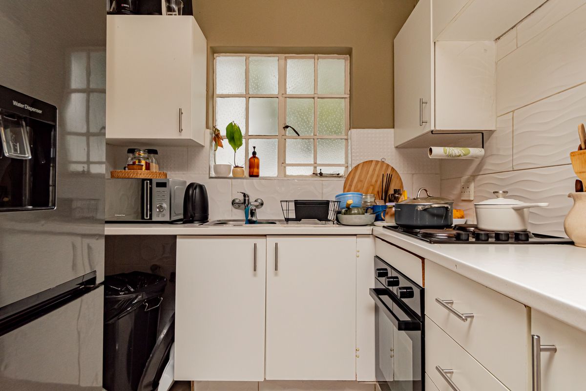 Compact kitchen featuring white cabinetry, laminate countertops, a built-in oven with gas hob, and a tiled backsplash with a window for natural light.