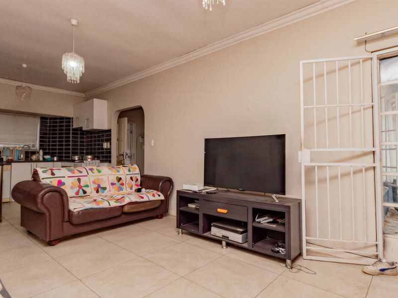 Open-plan living area featuring tiled floors and an integrated kitchen space with cabinetry, leading to an exterior access point with a security gate.