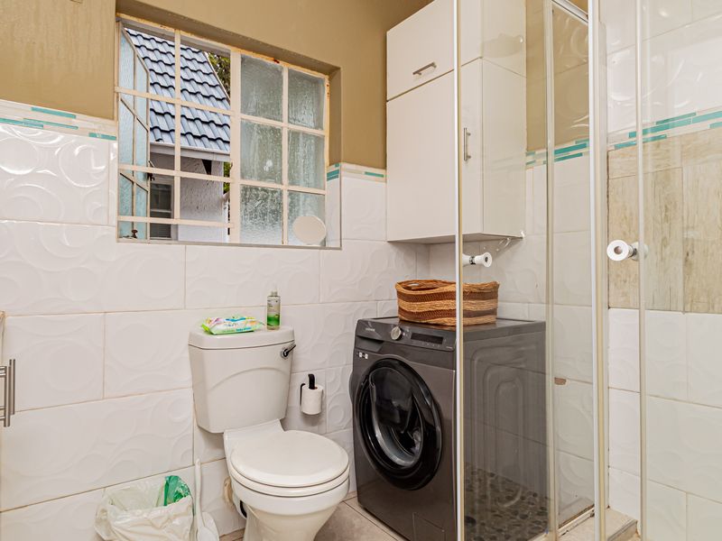 A functional bathroom featuring a shower enclosure, toilet, and wall-mounted storage cabinetry with tiled wall finishes.
