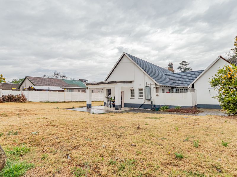 Rear view of the house featuring a covered patio, paved area, and a large garden enclosed by a perimeter wall.