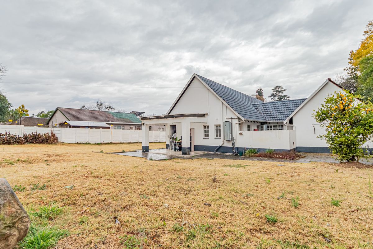 Rear view of the house featuring a covered patio, paved area, and a large garden enclosed by a perimeter wall.