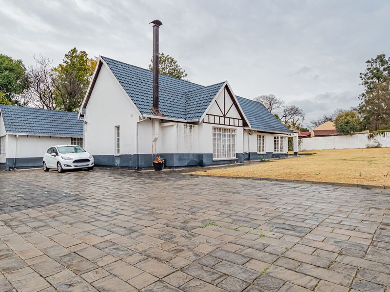 Front view of a detached house featuring a tiled roof, chimney, and extensive paved driveway area with surrounding garden space.