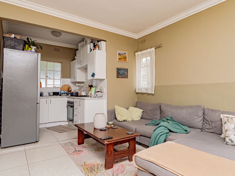 Open-plan living area featuring a compact kitchen with built-in cabinetry and oven, seamlessly connected to a comfortable lounge space with tiled flooring.