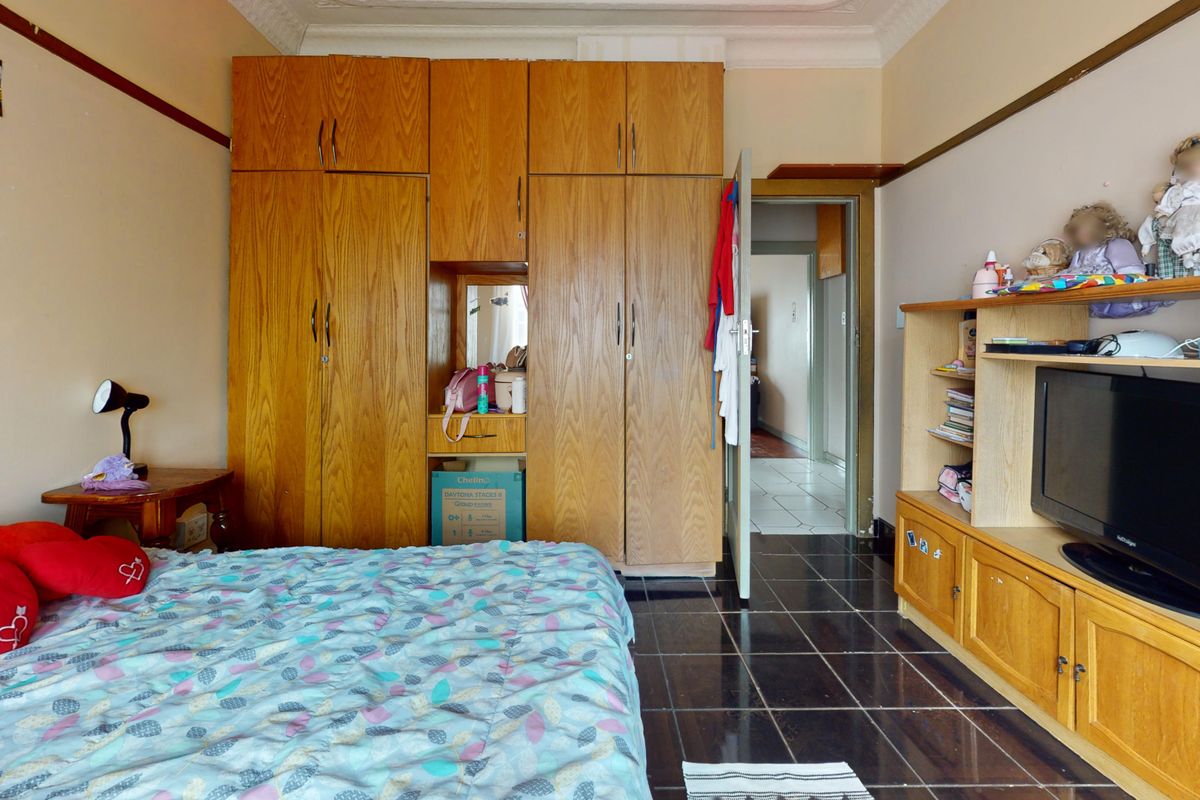A bedroom featuring built-in wooden cupboards, dark tiled flooring, and decorative ceiling cornicing.