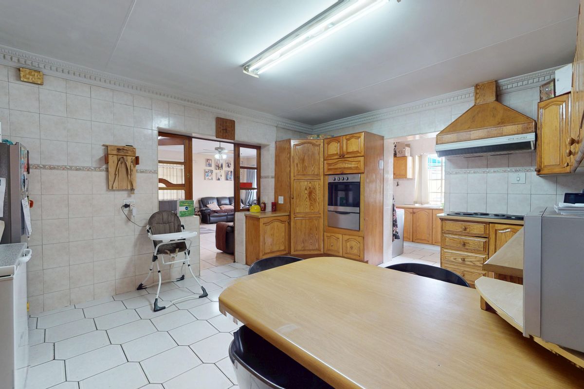 A functional kitchen featuring traditional wooden cabinetry, built-in oven, extractor fan, and tiled surfaces, with an open layout connecting to the adjacent living area.