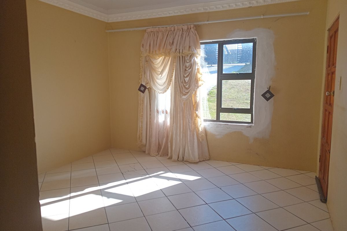 An empty living room featuring tiled flooring, decorative cornice, and a window with unfinished plasterwork, offering a blank canvas for renovation.