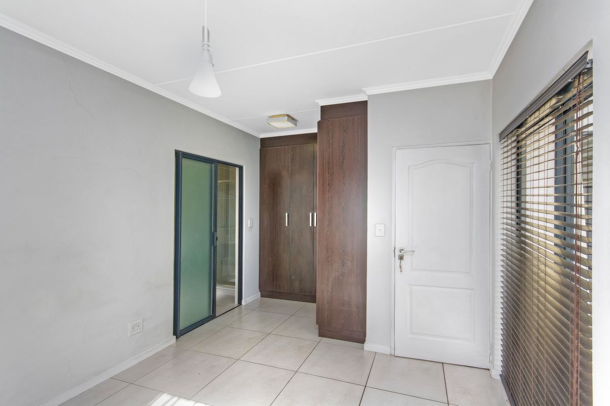 A bedroom featuring built-in dark wood cabinetry, tiled flooring, and a sliding door leading to an en-suite bathroom.