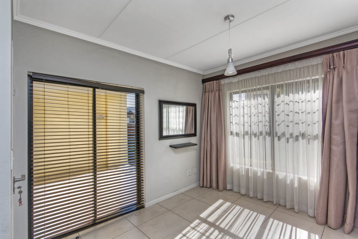 A bright living area featuring tiled flooring, a sliding glass door with blinds, and large windows with curtains, providing access to an outdoor space.
