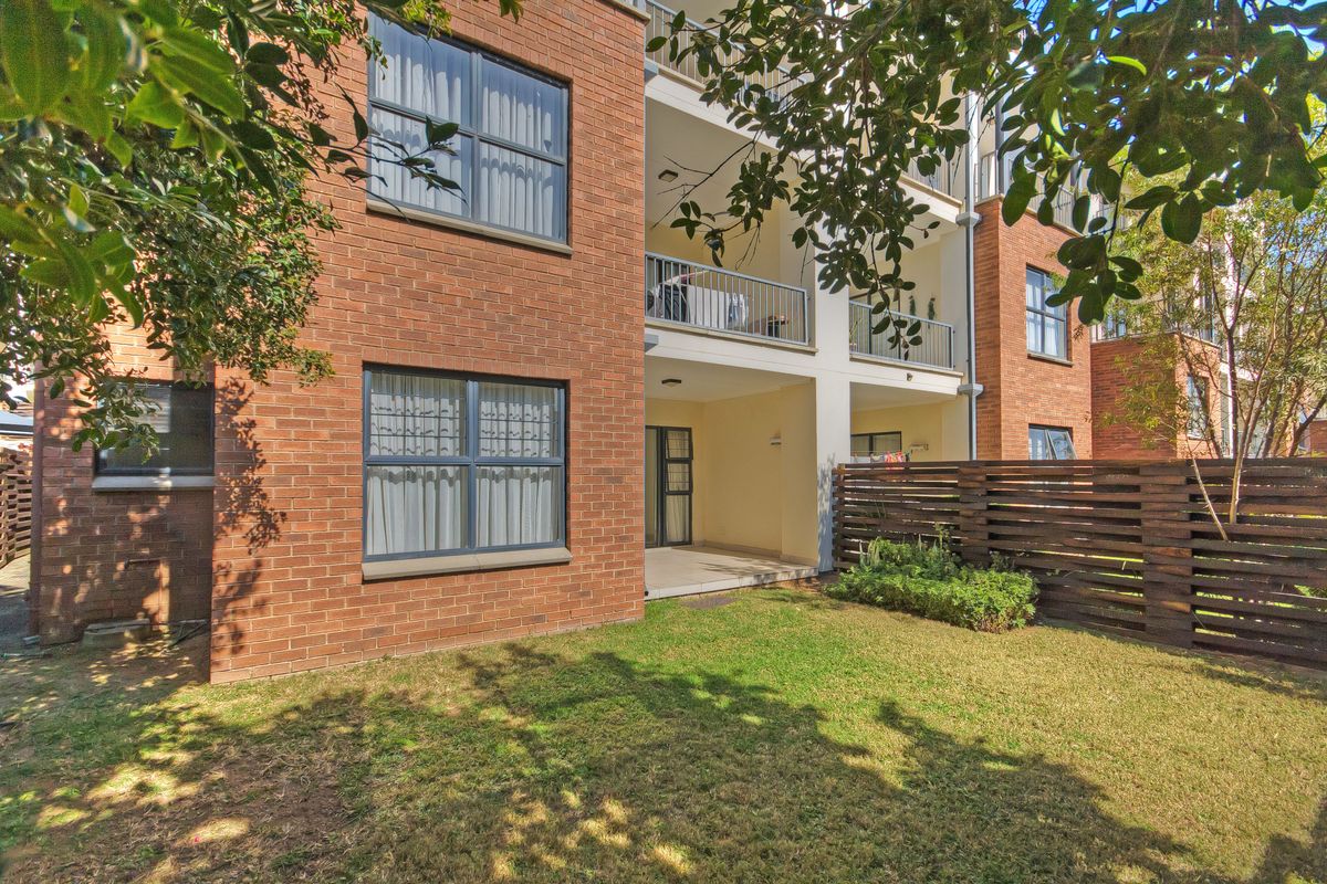 A view of the apartment building exterior featuring a private ground floor patio, small garden area, and brick facade construction.