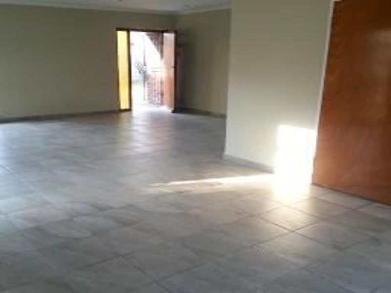 A spacious, empty living area featuring neutral tiled flooring and a wooden door leading to the exterior.