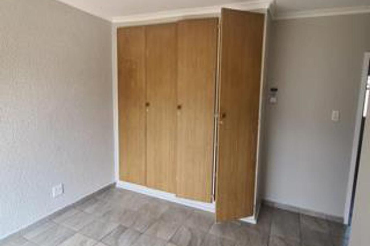 An empty bedroom featuring tiled flooring and built-in wooden cupboards with some visible wear.