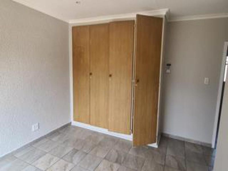 An empty bedroom featuring tiled flooring and built-in wooden cupboards with some visible wear.