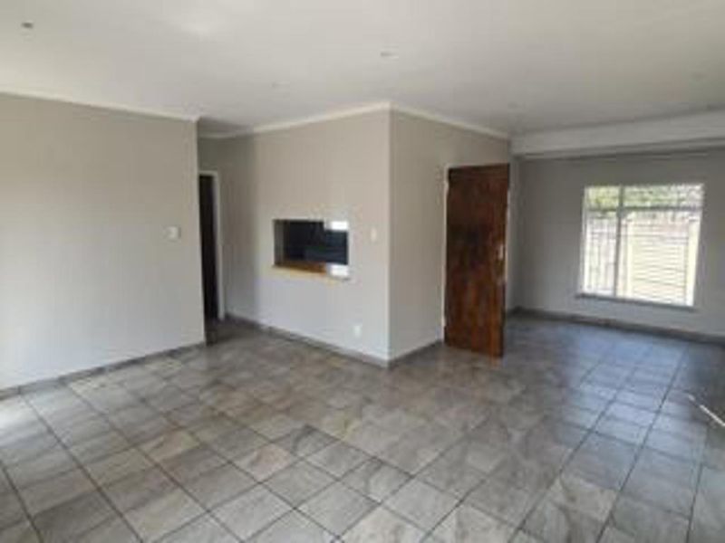 A spacious, empty living area featuring neutral wall tones, tiled flooring, recessed lighting, and a convenient serving hatch connecting to the kitchen area.