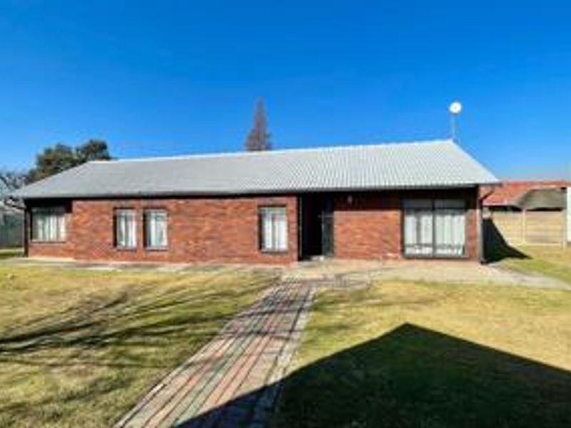 Rear view of a single-story brick house featuring a corrugated metal roof, paved walkway, and sliding glass doors leading to the garden.