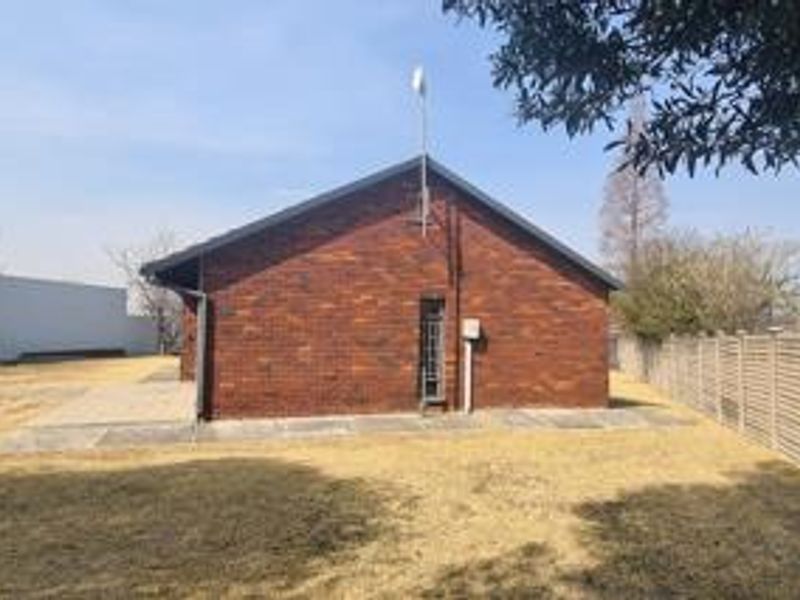 Rear view of the property featuring a face brick facade, pitched roof, and a paved patio area set within a fenced garden.
