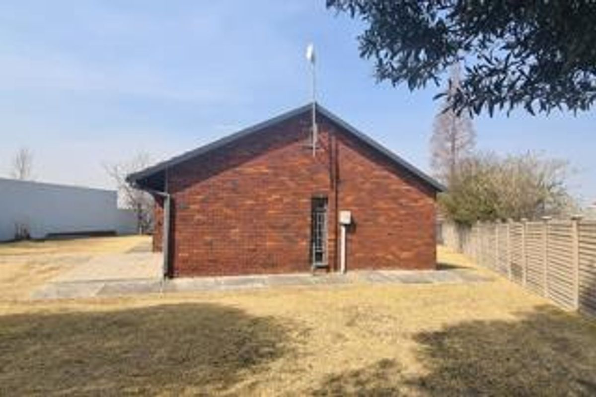Rear view of the property featuring a face brick facade, pitched roof, and a paved patio area set within a fenced garden.