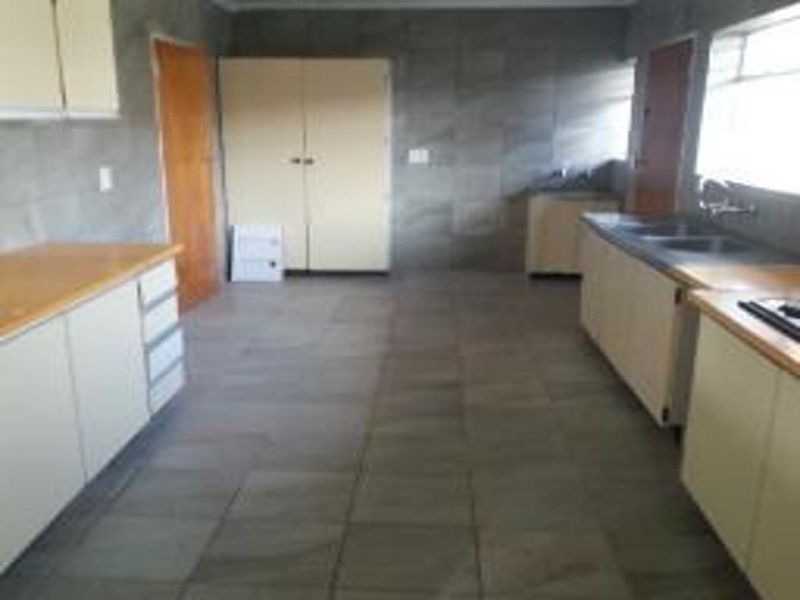 A spacious, empty kitchen featuring tiled walls and floors, ample built-in cabinetry, and laminate countertops, offering a blank canvas for renovation.