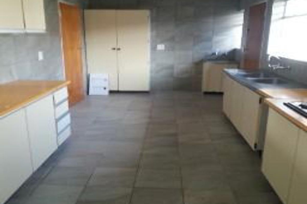 A spacious, empty kitchen featuring tiled walls and floors, ample built-in cabinetry, and laminate countertops, offering a blank canvas for renovation.