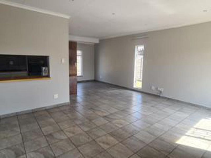 A spacious, empty living area featuring neutral wall tones, tiled flooring, and a convenient serving hatch connecting to the kitchen space.