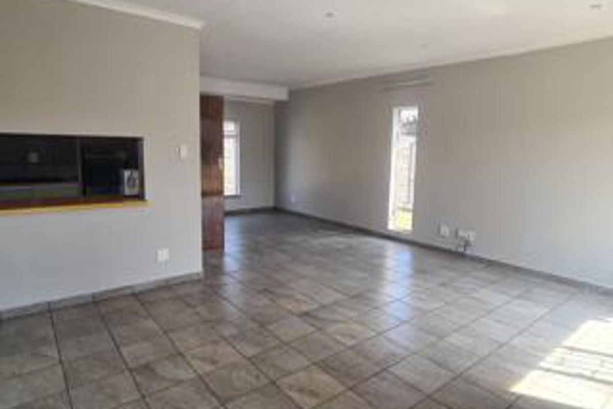 A spacious, empty living area featuring neutral wall tones, tiled flooring, and a convenient serving hatch connecting to the kitchen space.