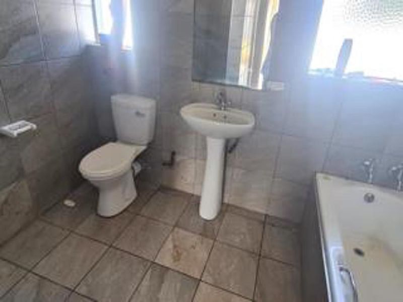 A functional bathroom featuring a pedestal basin, toilet, and bathtub with full-height wall tiling and floor tiles.