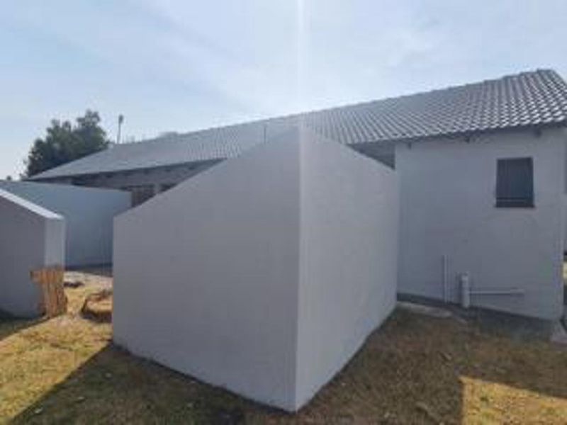 Rear view of the property showing the plastered exterior walls, tiled roof, and surrounding yard area.