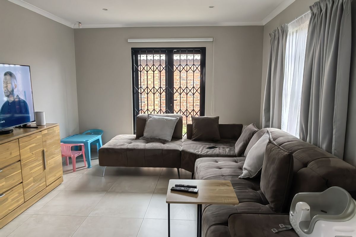 A well-maintained living room featuring neutral tiled flooring, recessed downlighting, and a secure metal gate leading to the exterior.
