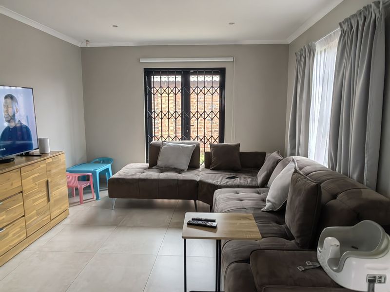 A well-maintained living room featuring neutral tiled flooring, recessed downlighting, and a secure metal gate leading to the exterior.