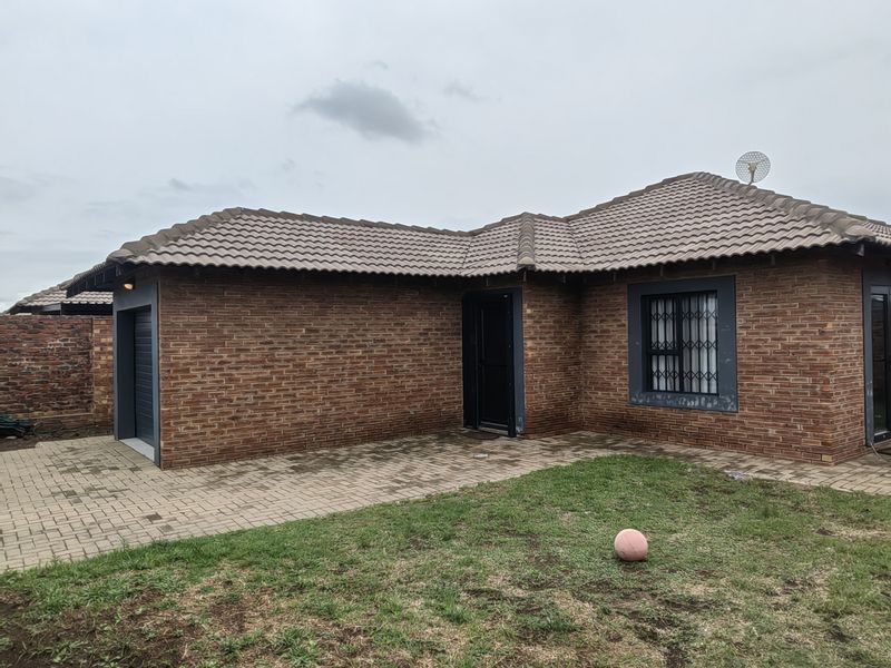 A single-story face brick house featuring a tiled roof, paved driveway, and integrated garage, set on a manageable residential plot.