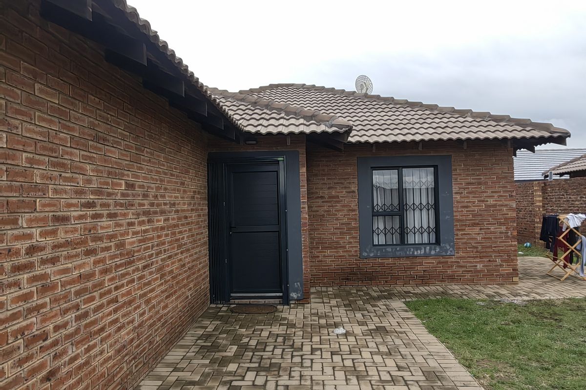 Rear exterior view of the house featuring a face brick facade, tiled roof, and a paved patio area.