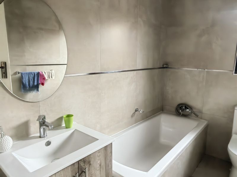 Modern bathroom featuring a built-in vanity with basin, a bathtub, and neutral wall tiling.