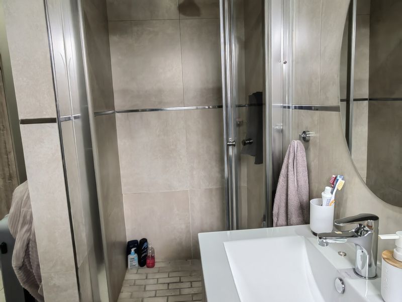 Modern bathroom featuring a tiled shower enclosure with glass door, a sleek vanity basin with mixer tap, and a large round wall mirror.
