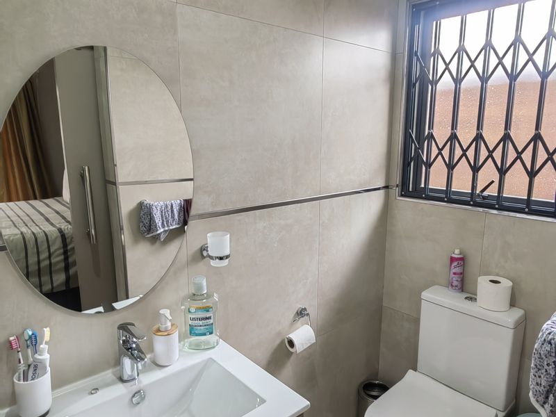 A modern bathroom featuring a vanity cabinet with a basin, a circular mirror, and a toilet, finished with neutral wall and floor tiles.