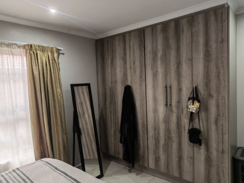 A well-maintained bedroom featuring modern wood-grain built-in cupboards, neutral tiled flooring, and coved ceiling details.